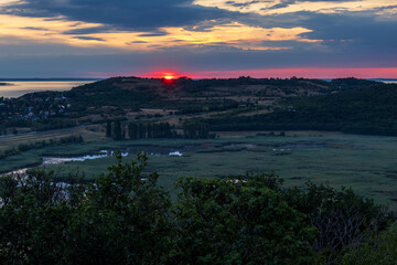 Scenic sunrise view of the Tihany Outer Lake with reed beds, showing the half-risen sun above the...