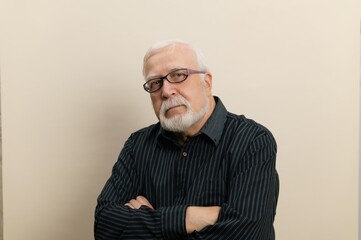 Senior man with white beard and glasses wearing striped shirt poses confidently against neutral...