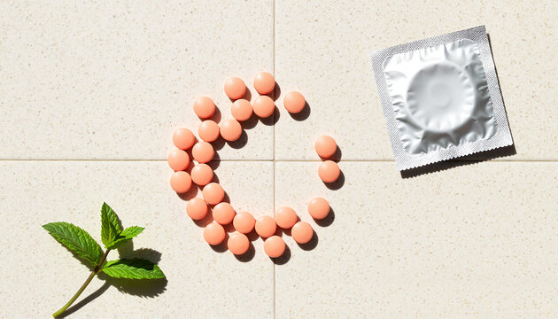 Pink pills and condom arranged on tile surface with mint leaf   - Powered by Adobe