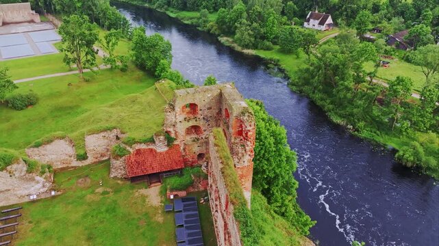 Drone of ruined tower of Bauska Castle beside Memele River as bird glides by