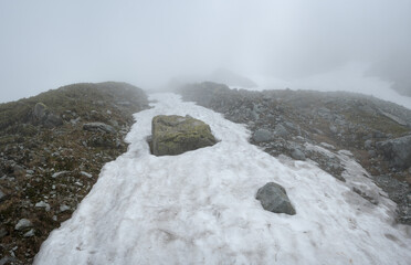A foggy high-mountain trail among large boulders and dangerous rocks.
