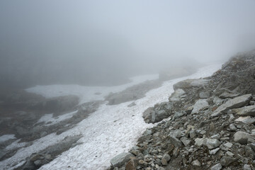 A foggy high-mountain trail among large boulders and dangerous rocks.
