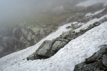 A foggy high-mountain trail among large boulders and dangerous rocks.
