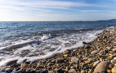 Waves wash over smooth and textured stones along a beautiful coastline. The calm waters reflect...