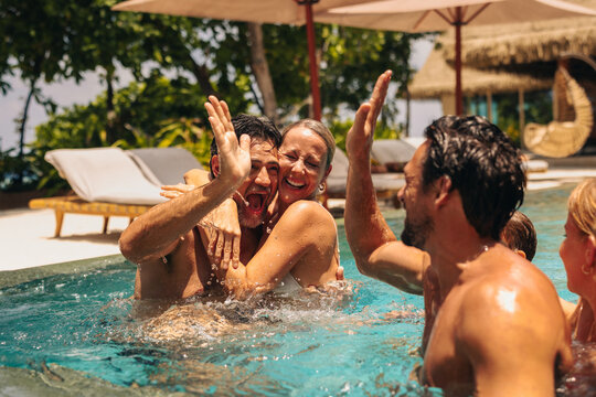 Joyful group of friends sharing a high-five in pool on sunny holiday getaway