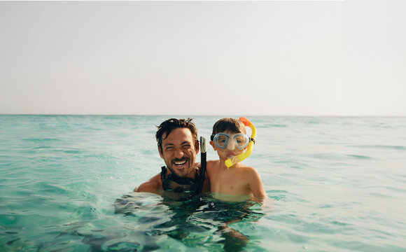 Father and son snorkeling with goggles and smiling in the clear sea