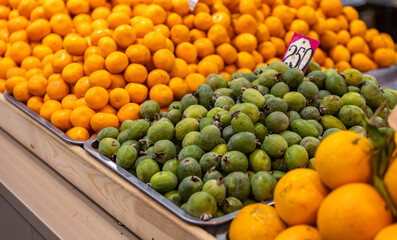 A vibrant display of fresh green feijoas stacked in a market, contrasting with bright orange fruits...