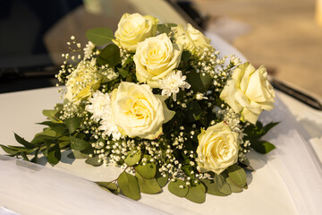 A stunning arrangement of white roses and delicate blossoms rests on the hood of a car, bathed in golden sunlight, signaling love and celebration at a joyful wedding event.