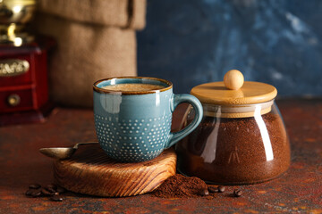 Jar with coffee powder and cup on brown table near blue wall, closeup