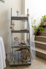 A rustic three-tier shelf adorned with delicate flowers and soft white draping, creating an...
