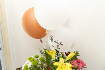 Decorative balloons and vibrant flowers create a festive atmosphere at a bridal shower. The scene...