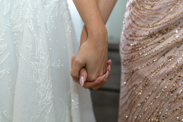 Two brides stand side by side, holding hands with grace and anticipation. The shimmering dresses...