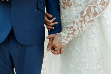 A couple stands side by side, their fingers gently interlocked, showcasing a moment of intimacy and...