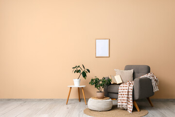 Comfortable grey armchair with soft pouf and houseplants near beige wall