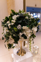 A beautiful display of fresh white flowers and lush greenery arranged elegantly in a chic metallic vase. This centerpiece adds a touch of sophistication to the wedding reception ambiance.