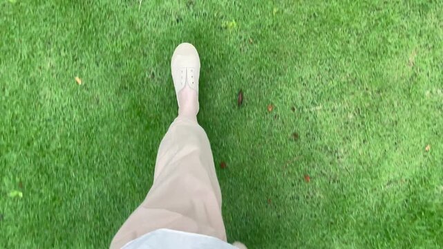 POV walking video (horizontal): First person view of a person wearing a light casual minimalist outfit walking on green grass in a sunny park, capturing relaxed, carefree and natural outdoor style.