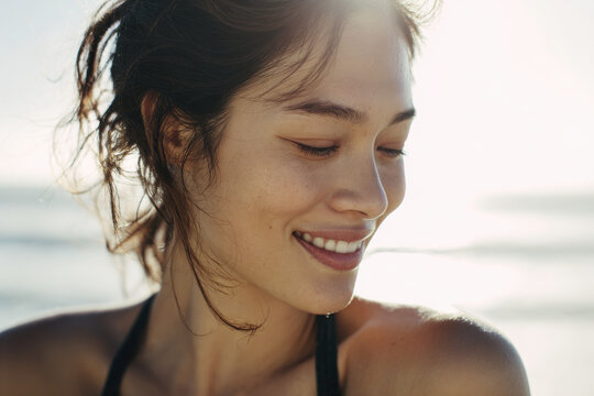 young woman smiles gently with her head bowed after refreshing stretch on beach