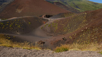 Rugged volcanic landscape with large, rust-colored rock, and cinder cone and volcanic crater....