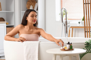 Pretty young woman sitting in bathtub and taking bath bomb at home