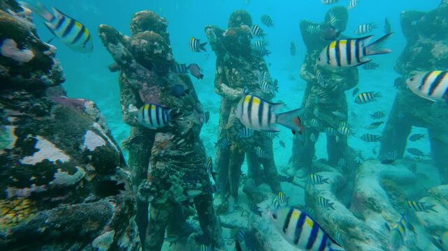 Underwater statues at Gili Meno, Indonesia, surrounded by tropical fish and coral in clear ocean. Famous snorkeling and diving site in Asia, combining marine life, art, and exotic travel.