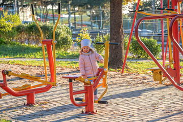 A young child plays on colorful outdoor fitness equipment in a park during autumn, enjoying a fun and healthy recreational activity in nature.