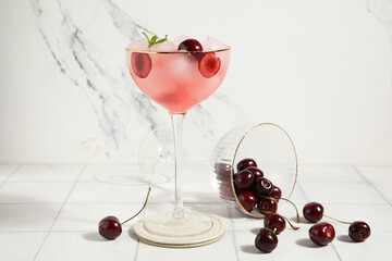Glass of drink with cherries, ice cubes and mint leaves on tile table against marble wall