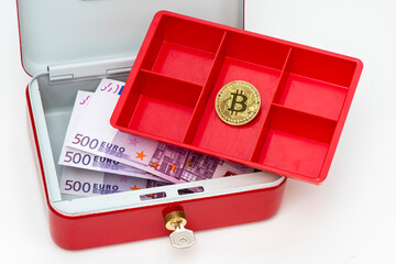 In einer Geldkassette liegen einige Bündel mit Euro Geldscheinen und eine Münze Bitcoin