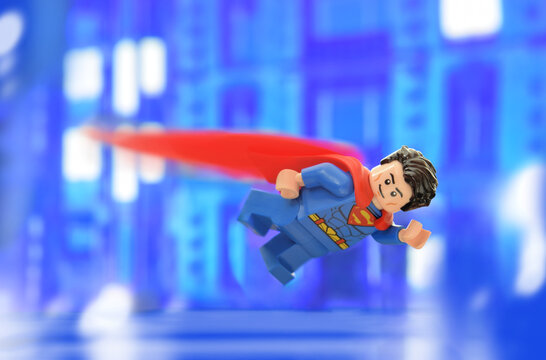 Lego minifigure of Superman in costume is flying in darkness on town or city. Editorial illustrative image of popular children toys.
