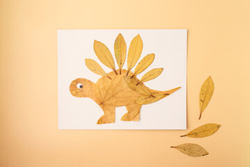 Handmade dinosaur from dried leaves on paper, kids craft flat lay with copy space, autumn activity...