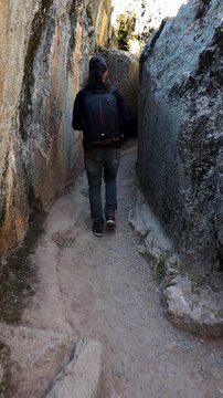 A young man walks through the ancient stone pathways of the Qenqo archaeological complex in Cusco, Peru. The footage captures the historic atmosphere and impressive stonework of the Inca ruins.