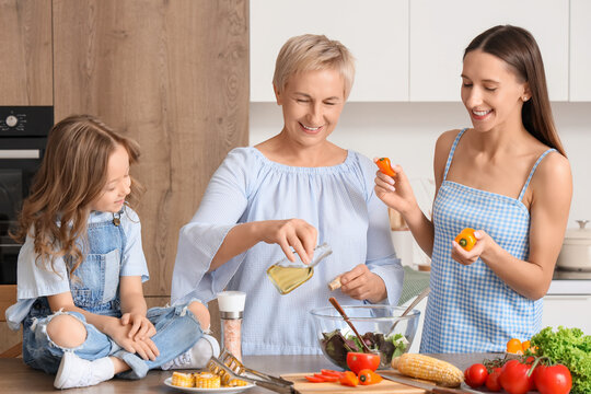 Little girl with her mother and granny making vegetable salad at table in kitchen - Powered by Adobe