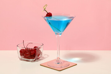 Glass of tasty Blue Lagoon cocktail garnished with cherry on white table against pink background