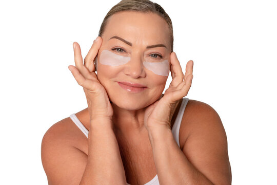 Woman applying under-eye patches while smiling in a serene indoor setting during daylight hours to enhance skin care routine