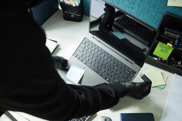Black gloved hands of anonymous man inserting USB flash device with malware into laptop, while...
