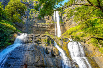 A tiered waterfall cascades down a rocky cliff, surrounded by lush green trees
