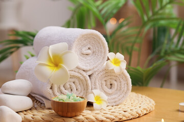 Towels with spa stones, candles, white plumeria flowers and sea salt on table in salon