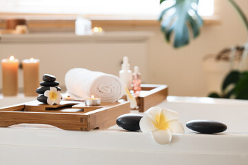 Towel with candles, spa stones and white plumeria flowers on stand in bathtub at salon