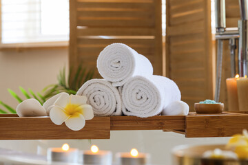 Towels with candles, sea salt and white plumeria flowers on stand in bathtub at salon