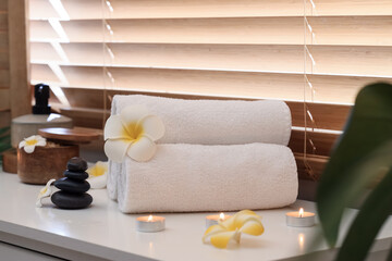Towels with candles, spa stones and plumeria flowers on windowsill in salon