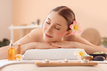 Beautiful young happy woman with pink plumeria flowers, sea salt, candles and cosmetic oil lying on...