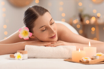 Beautiful young happy woman with pink plumeria flowers and candles lying on couch in spa salon