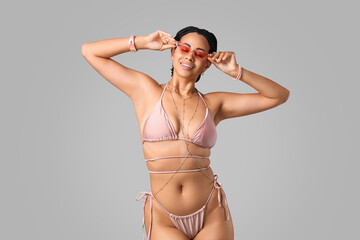 Pretty young African-American woman in bikini with accessories and sunglasses on white background