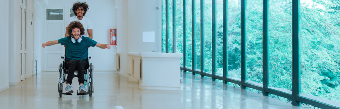 Two young friends enjoying playful wheelchair ride in modern hallway with large windows and natural light