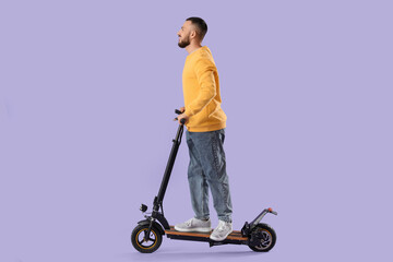 Young man riding electric kick scooter on lilac background