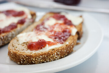 Close-up of whole grain bread with cream cheese and strawberry jam on white plate