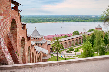 Historic kremlins red brick walls stretch beside river. Arched structures and lush greenery create...