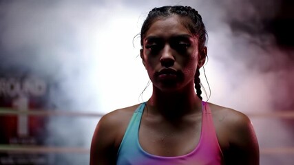 determined hispanic female boxer standing confidently in dimly lit boxing ring with smoky atmosphere. intense focus and readiness for action. sports, fitness motivation, training session, athleticism - Powered by Adobe