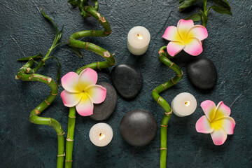 Beautiful spa composition with stones, plumeria flowers, green twigs and burning candles on dark...