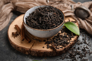 Bowl with dry black tea leaves and cinnamon on dark background, closeup