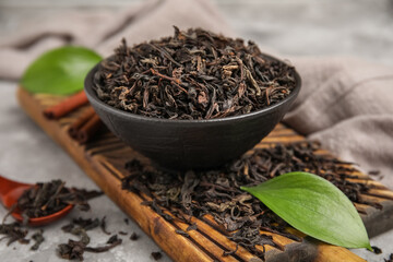 Bowl and wooden spoon with dry black tea leaves on grey background, closeup